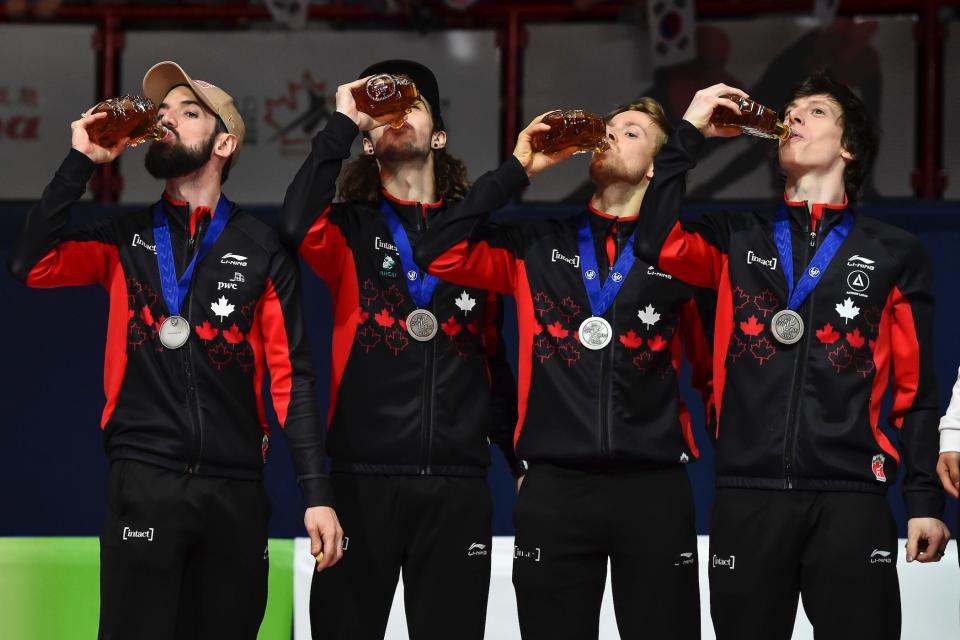 4 members of team canada with medals on, drinking maple syrup