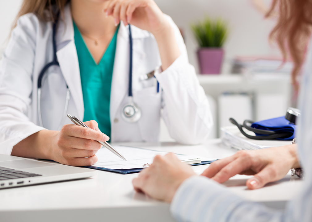 Doctor listening to patient, both sitting at a desk.