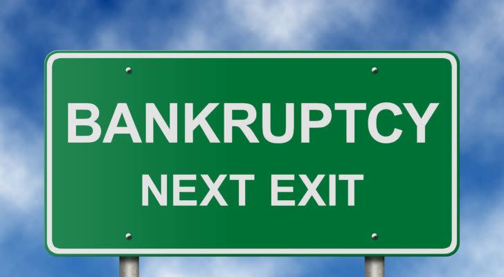 A green road sign reads "Bankruptcy Next Exit" in front of a cloudy blue sky.