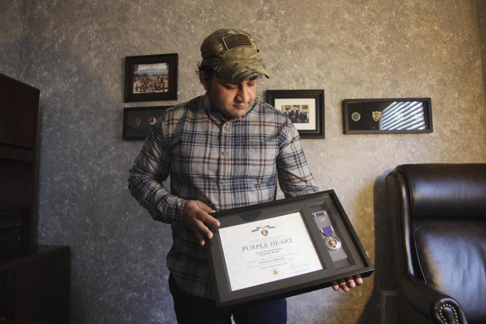 In this Monday, Dec. 16, 2019, photo, Zia Ghafoori displays the Purple Heart at his home in Charlotte, N.C., that he received while working with U.S. Forces in Afghanistan. Ghafoori was an interpreter and was wounded while fighting insurgents with U.S. Special Forces during the Battle of Shok Valley, Afghanistan. He received a Special Immigrant Visa in 2014 and is working toward becoming a U.S. citizen. (AP Photo/ Sarah Blake Morgan)