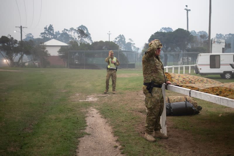 Members of a military support team deploy a tent as smoke begins to blanket the town of Eden