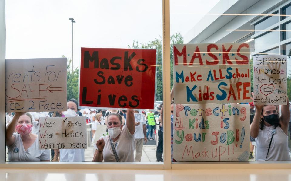 Pro-mask demonstrators hold signs against the windows of the Cobb County School District headquarters during a protest over their optional mask policy in Marietta, Georgia on 19 August 2021 - Elijah Nouvelage/Bloomberg