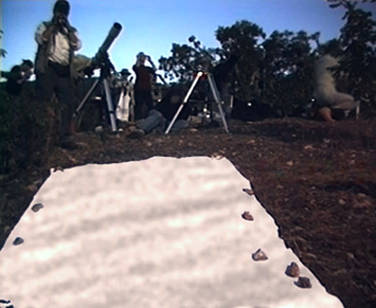 wavy lines of shadow on a sheet on the ground, with people and small telescopes in the background