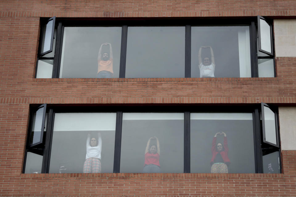 Residents take part in an aerobics class led by city police instructing from the street below during a lockdown ordered by the government in an effort to prevent the spread of the new coronavirus, in Bogota, Colombia, Friday, April 3, 2020. Colombian police visit neighborhoods inviting residents to their windows or balconies to participate in an aerobics class, and encourage social distancing. (AP Photo/Fernando Vergara)