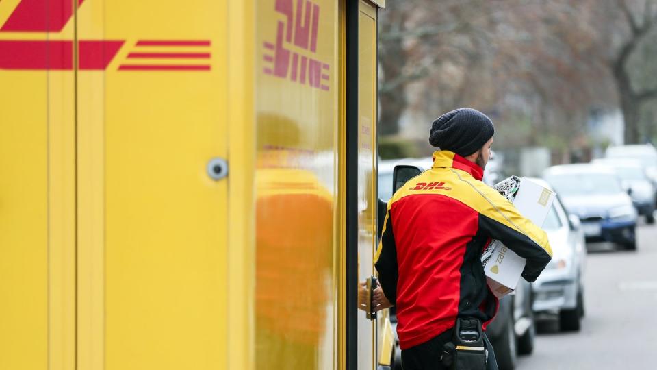 Ein DHL-Paketzusteller verlässt mit mehreren Sendungen sein Fahrzeug.