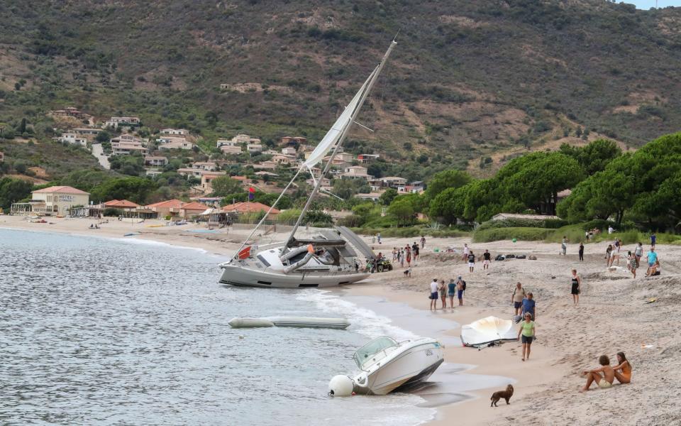 Bystanders look on at boats thrown onto the beach of Sagone in Coggia