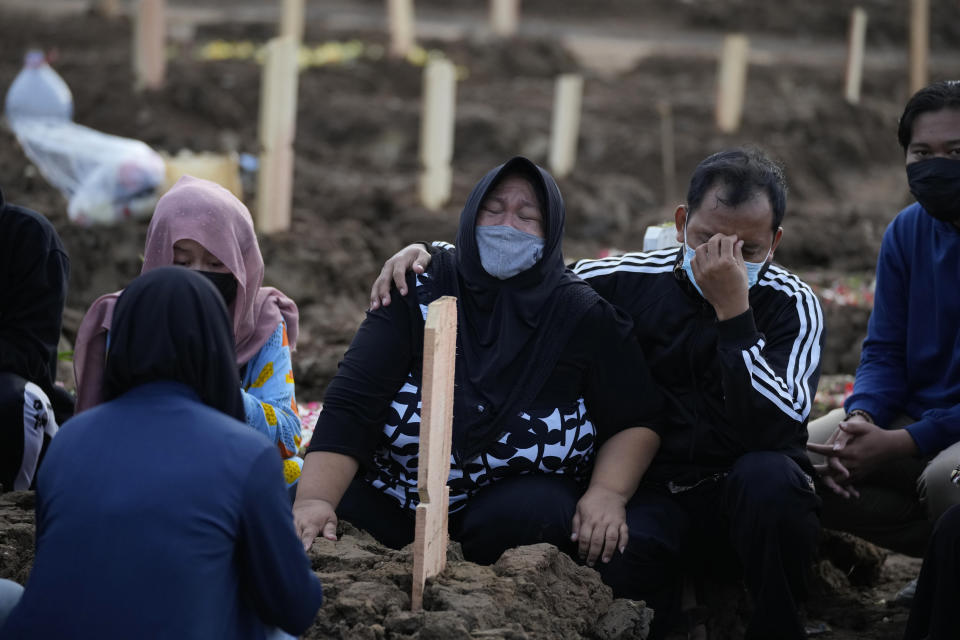 Family members weep during the burial of a relative at Rorotan Cemetery which is reserved for those who died of COVID-19, in Jakarta, Indonesia, Thursday, July 1, 2021. New land around the capital city continues to be cleared for the dead and gravediggers have to work late shifts following surges in COVID-19 cases fueled by travel during the Eid holiday in May, and the spread of the delta variant of the coronavirus first found in India. (AP Photo/Dita Alangkara)