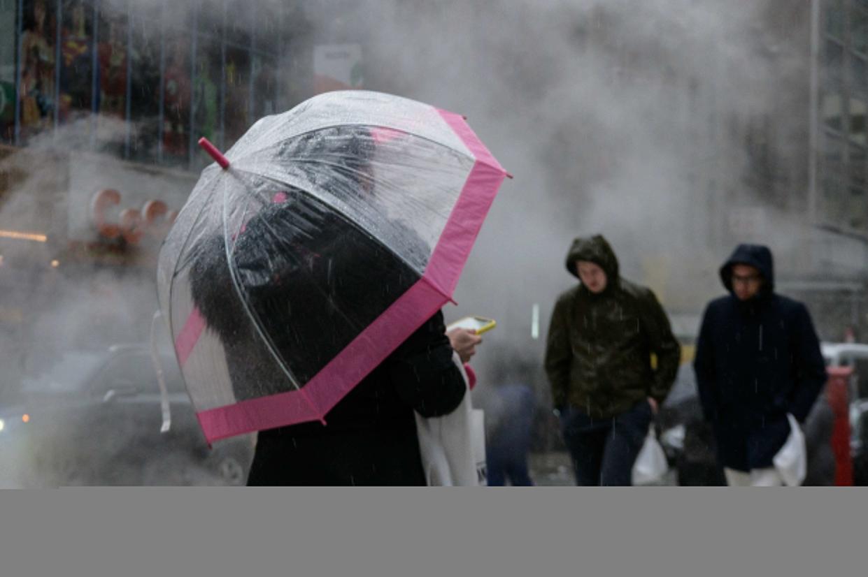 Pedestrians walk through steam on a rainy day in New York City.