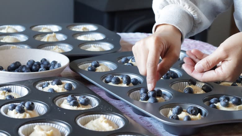 Person putting blueberries in muffin tin