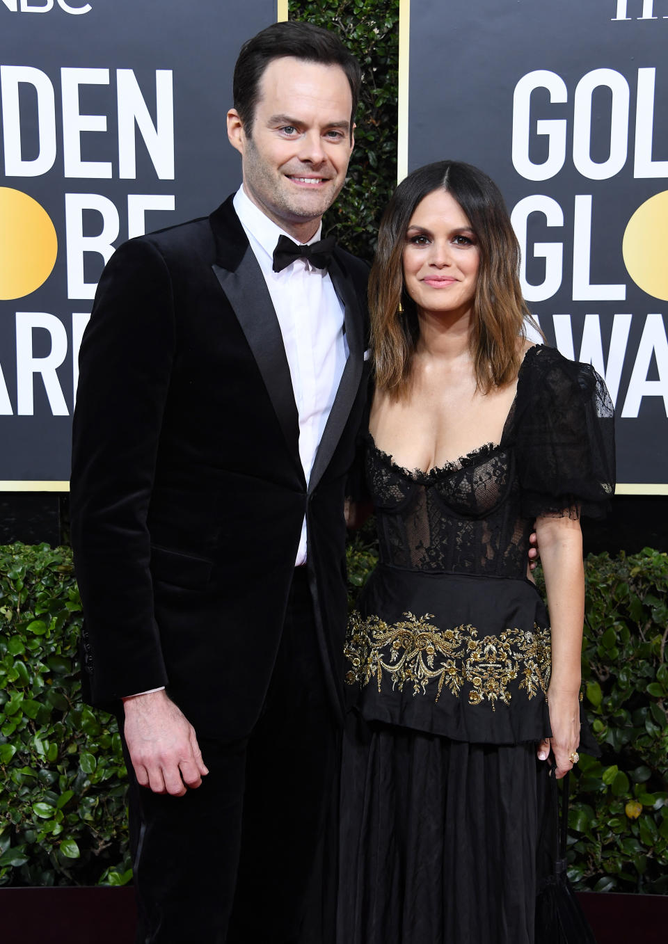 Man in black tuxedo and woman in ornate black dress with sheer details pose together at the Golden Globes