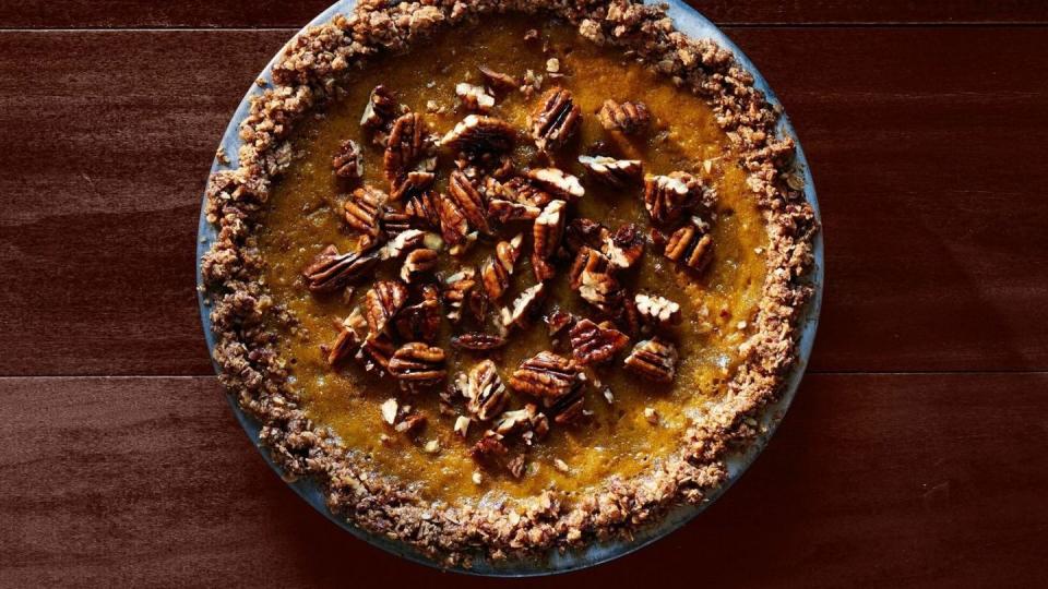 pumpkin pie with oat pecan crust in a metal pie plate with chopped pecans on top