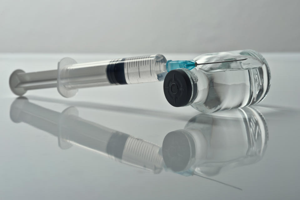 Injectable medications in sealed vials and a disposable plastic medical syringe against gray background.Studio shot