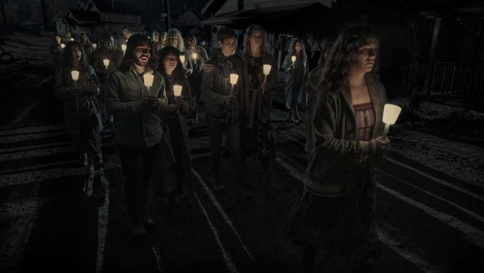 a woman leads a crowd of people holding candles in the dark