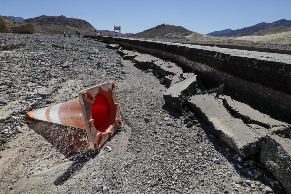 An orange traffic cone lays beside crumbled asphalt.