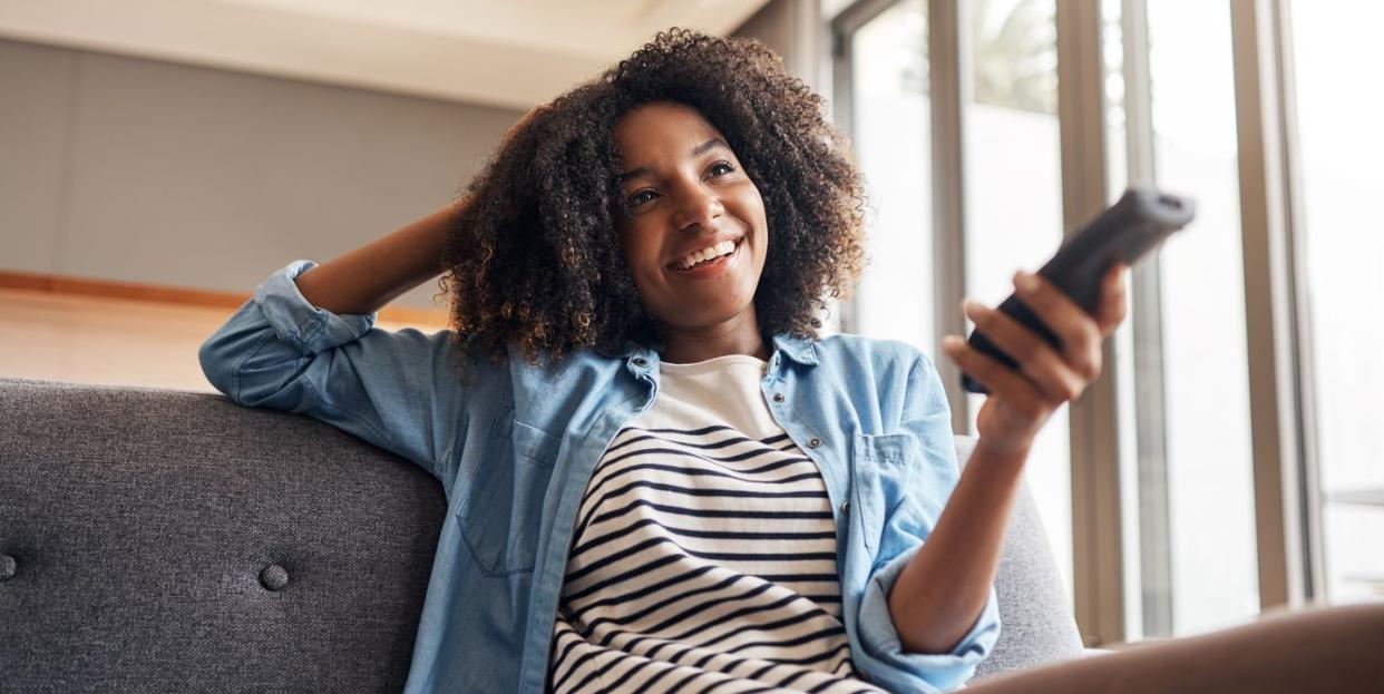 shot of a young woman holding a remote control while sitting on the sofa at home