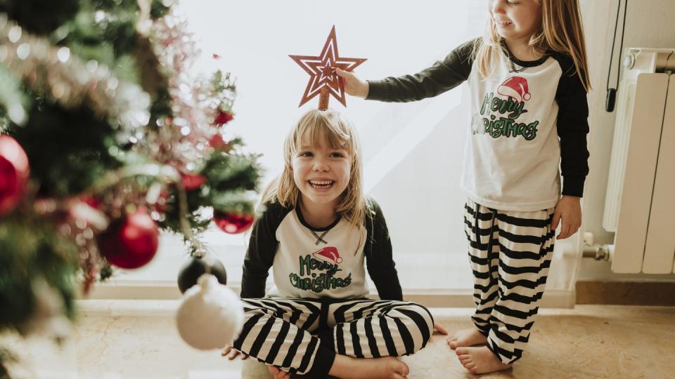 laughing sisters playing with christmas decoration against wall at home