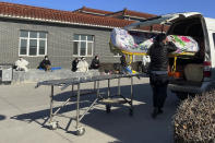 A man lifts an empty casket onto a van as relatives in traditional Chinese funeral attires rest near the Gaobeidian Funeral Home in northern China's Hebei province, Thursday, Dec. 22, 2022. Bodies from Beijing, a two-hour drive away are appearing at the Gaobeidian funeral home, because similar funeral homes in Beijing were packed. (AP Photo)