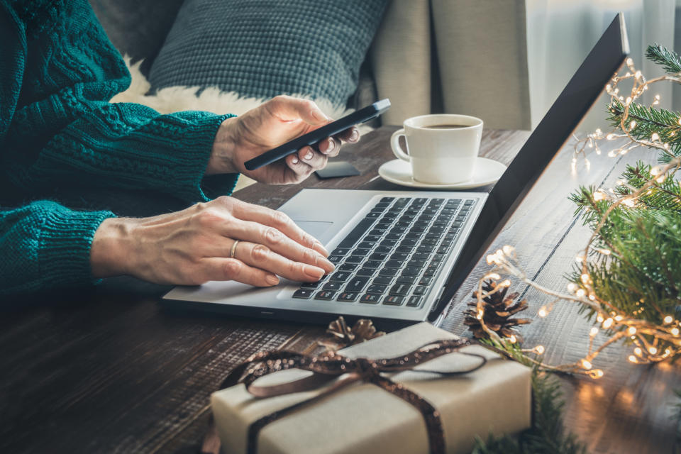 Christmas sales. Woman shopping with smartphone by laptop in home interior. Xmas concept. Planning holidays.