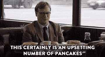 A bespectacled man in a suit comments on his assignment to eat 15 consecutive pancakes