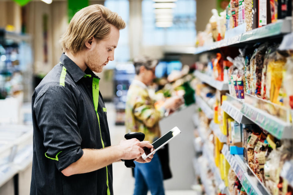 A supermarket employee doing his jobs performing a stock check using a bar code reader and a digital tablet.