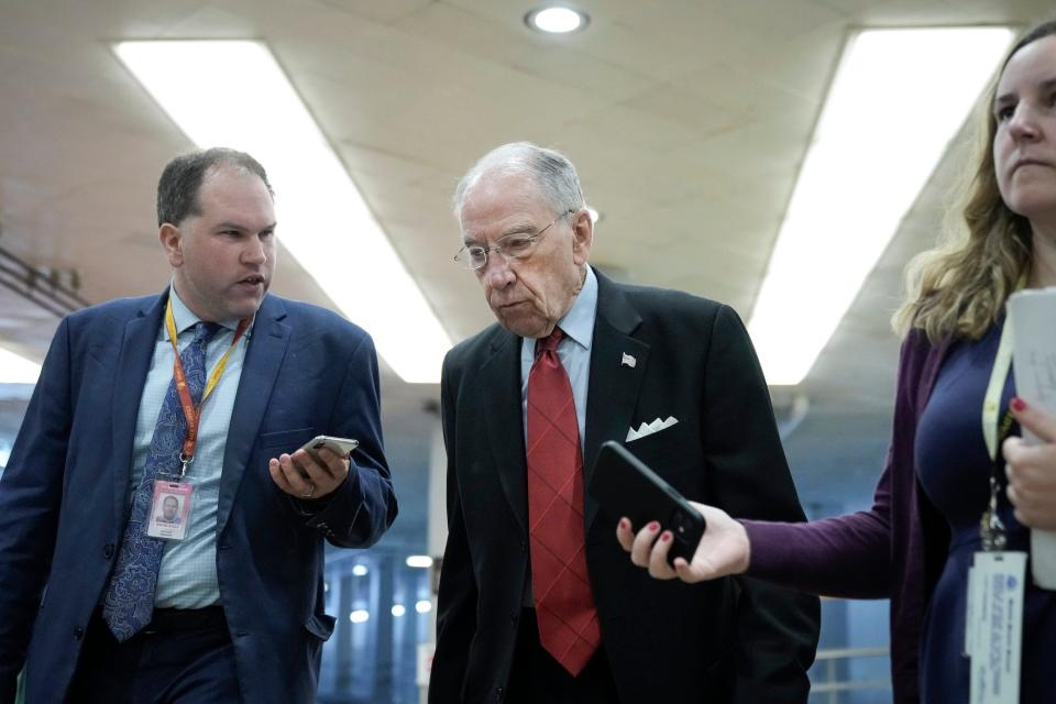 Republican Sen. Chuck Grassley of Iowa, who appears to be slightly hunched while sporting glasses, a dark suit jacket, and a bright red tie, speaks to a reporter while walking through the Senate subway on Capitol Hill.