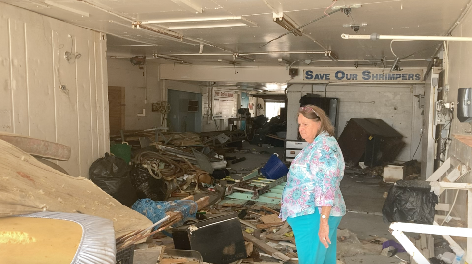 Historian and environmental education nonprofit Ostego Bay Environmental, Inc. founder Joanne Semmer stands in the wreckage of what was Trico Shrimp Company. Behind her, a sign reads 