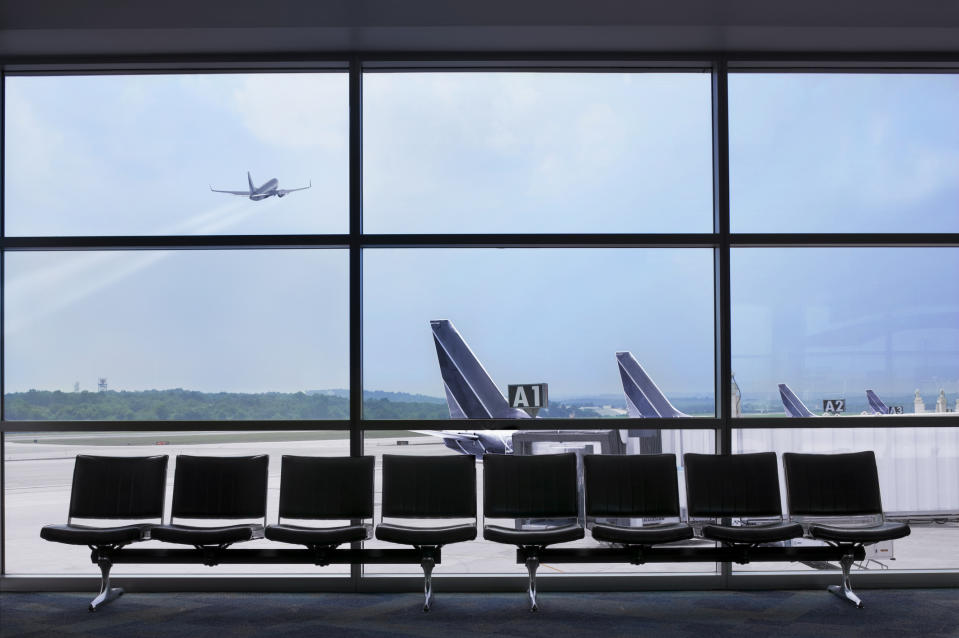 Empty airport seating with a view of a plane taking off outside the window