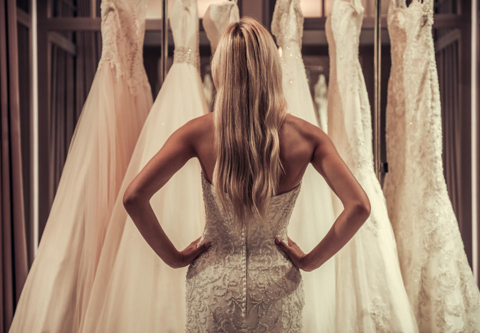 Back view of attractive young bride choosing wedding dress in modern wedding salon