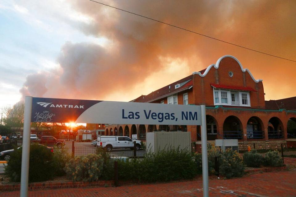 A sunset seen through a wall of wildfire smoke from the Amtrak train station in Las Vegas, N.M., on Saturday, May 7, 2022. The CastaÃ±eda Hotel, right, hosted meals for residents and firefighters this week with sponsorships from restaurants and other businesses.