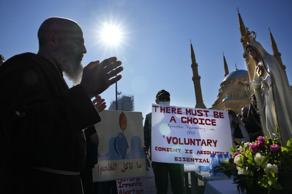 A priest and other protesters pray during a rally to protest measures imposed against people who are not vaccinated, in Beirut, Lebanon, Saturday, Jan. 8, 2022. Vaccination is not compulsory in Lebanon but in recent days authorities have become more strict in dealing with people who are not inoculated or don’t carry a negative PCR test. (AP Photo/Hussein Malla)