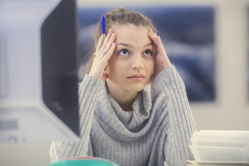 Portrait of young woman at desk in an office looking concerned.