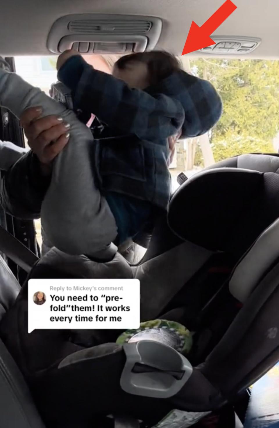 Person struggles to fit stroller in car trunk without bumping the child's head