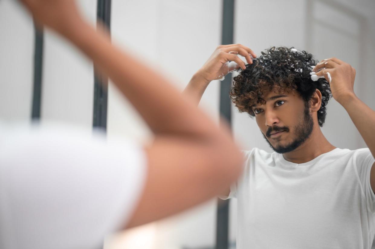 Portrait of a serious young Indian man applying the foaming mousse to his curly hair