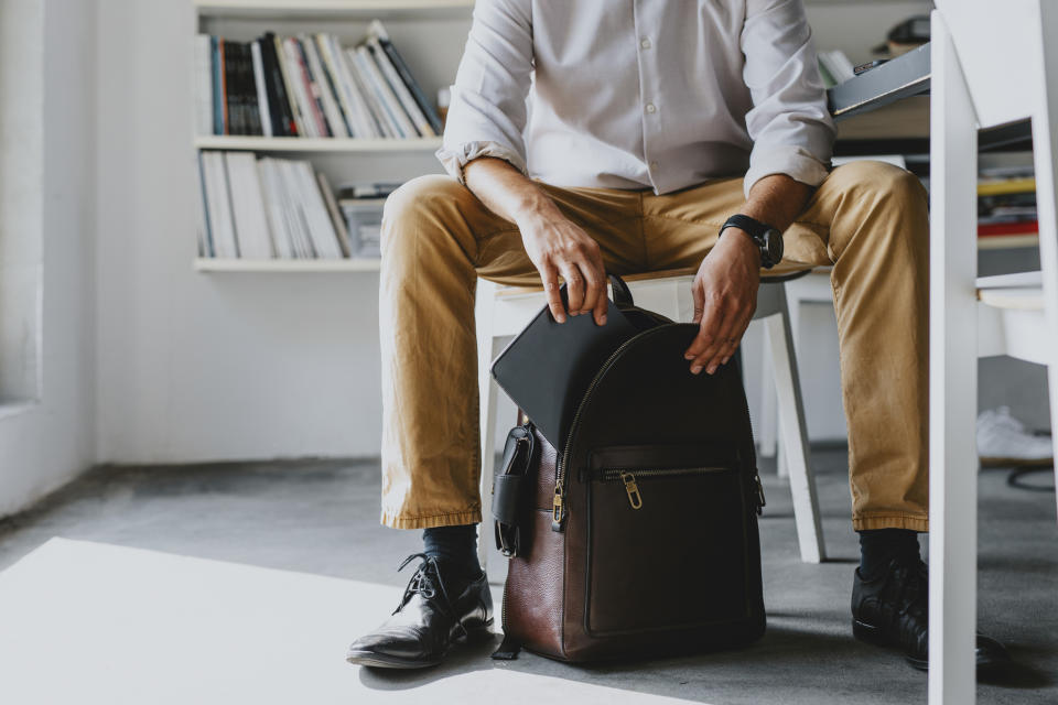 Person sitting with a leather bag between their legs, dressed in smart casual attire suitable for a professional setting