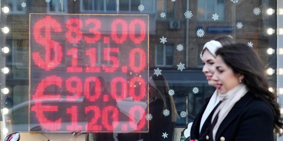 People walk past a currency exchange office screen displaying the exchange rates of U.S. Dollar and Euro to Russian Rubles in Moscow's downtown, Russia.