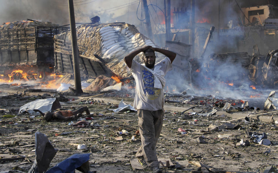 FILE -bIn this Saturday, Oct 14, 2017, file photo, a man walks past a dead body and destroyed buildings at the scene of a blast in the capital Mogadishu, Somalia. Somalia is marking the first anniversary of one of the world's deadliest attacks since 9/11, a truck bombing in the heart of Mogadishu that killed well over 500 people. The Oct. 14, 2017 attack was so devastating that the al-Shabab extremist group that often targets the capital never claimed responsibility amid the local outrage. As Somalis gather at a new memorial with a minute of silence, local media report that the man accused of orchestrating the bombing has been executed. (AP Photo/Farah Abdi Warsameh, File)