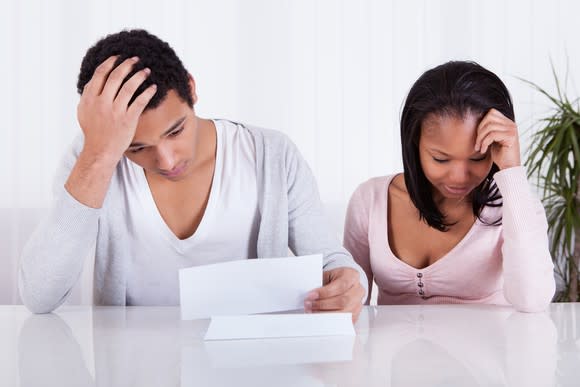 A couple looking worried with head in hands while looking at papers.