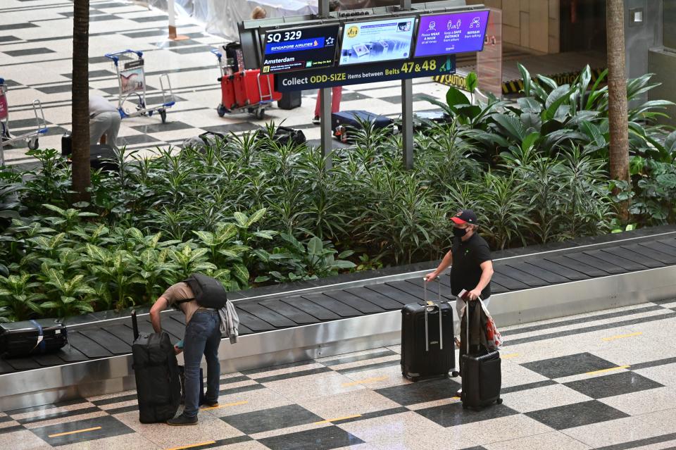 Passengers arriving from Amsterdam get their bags at Changi Airport in Singapore on October 20, 2021, a day after the country began quarantine-free entry for fully vaccinated passengers from eight countries, part of a plan to ease restrictions as the business hub gears up to live with the coronavirus. / AFP / Roslan RAHMAN