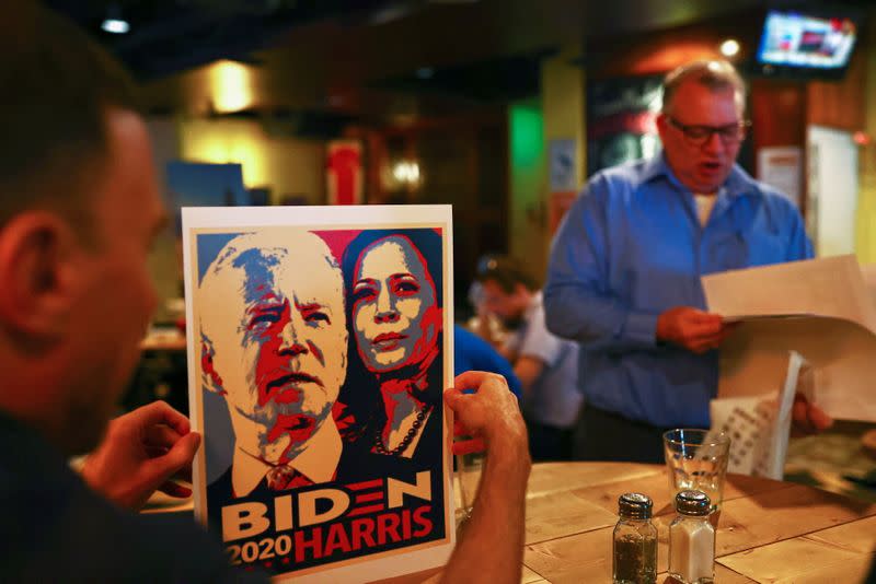 A man holds a poster with the image of U.S. Democratic presidential nominee Joe Biden and running mate, Senator Kamala Harris as others watch live results from the U.S. election at a bar in Taipei, Taiwan