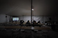 Workers watch TV and eat dinner in the cafeteria of a tent city for electrical workers in Amelia, La., Friday, Sept. 17, 2021. In one massive white tent, hundreds of cots are spread out; experienced workers bring their own inflatable mattresses. Another tent houses a cafeteria that serves hot breakfast starting about 5 a.m., dinner and boxed lunches that can be eaten out in the field. (AP Photo/Gerald Herbert)