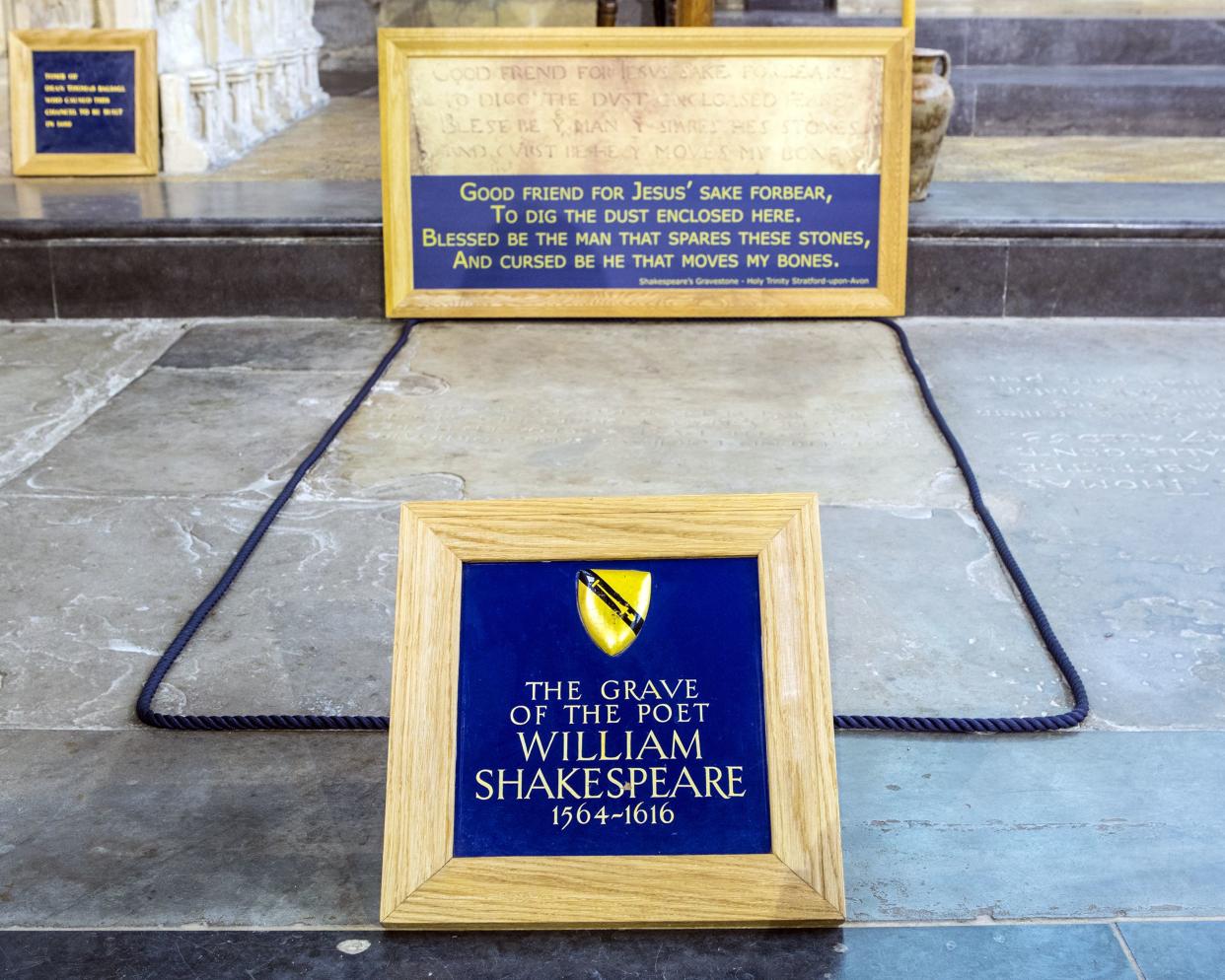William Shakespeare's simple stone grave in the Holy Trinity Church, Stratford-upon-Avon, England, a sign in a frame in the place of a headstone, with other such graves and an urn in the background