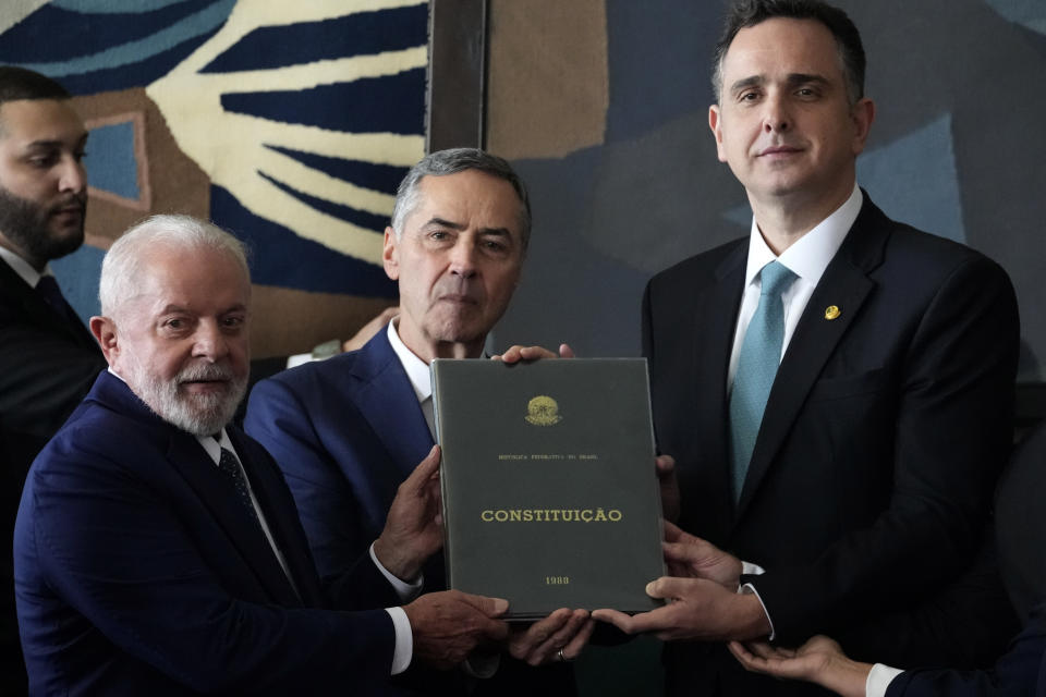 Brazilian President Luiz Inacio Lula da Silva, left, Senate President Rodrigo Pacheco, right, and Supreme Court President Luis Roberto Barroso hold a copy of their nation's Constitution at Congress in Brasilia, Brazil, Monday, Jan. 8, 2024. This copy of the magna carter was restored after being destroyed by rioters who stormed the presidential palace, Congress and the Supreme Court buildings one year ago in support of outgoing, former President Jair Bolsonaro who has been under investigation by the Supreme Court over his role in the mayhem. (AP Photo/Eraldo Peres)