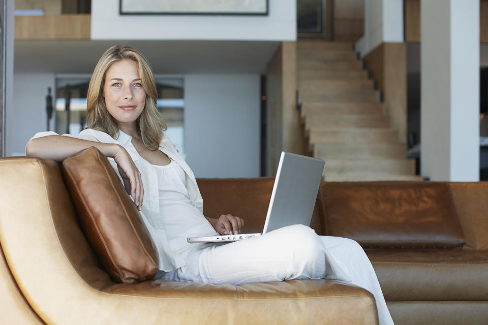 A woman sitting on her couch and smiling, with her laptop on her lap