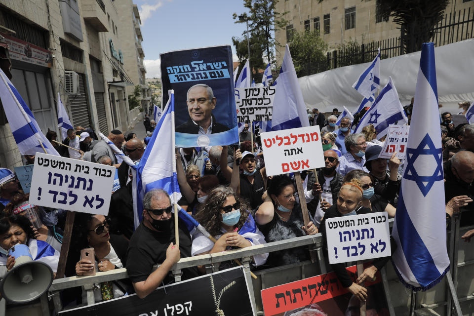 Israeli right wing activists hold flags and signs in support of Prime Minister Benjamin Netanyahu during a demonstration outside the Jerusalem district court In Jerusalem, Sunday, May 24, 2020. Israeli Prime Minister Benjamin Netanyahu was heading to court Sunday to face corruption charges in the first criminal trial ever against a sitting Israeli leader. Hebrew reads:"Netanyahu is not alone." (AP Photo/Sebastian Scheiner)