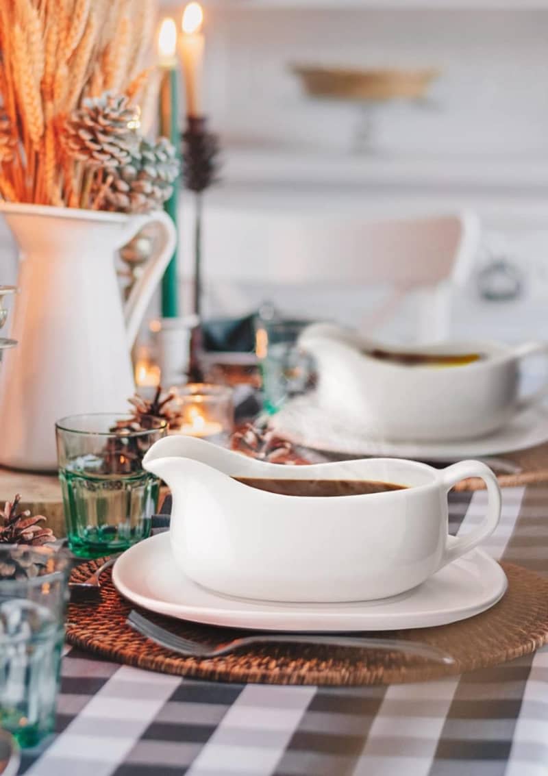 gravy boats on trays with buffalo check table cloth and warm lighting behind vase filled with wheat