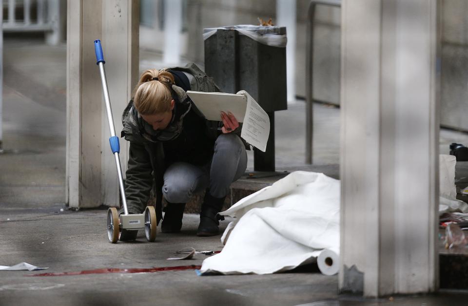 A police officer examines the crime scene next to a covered body following a shooting at the entrance of Building E of the courthouse in Frankfurt January 24, 2014. REUTERS/Ralph Orlowski (GERMANY - Tags: CRIME LAW)