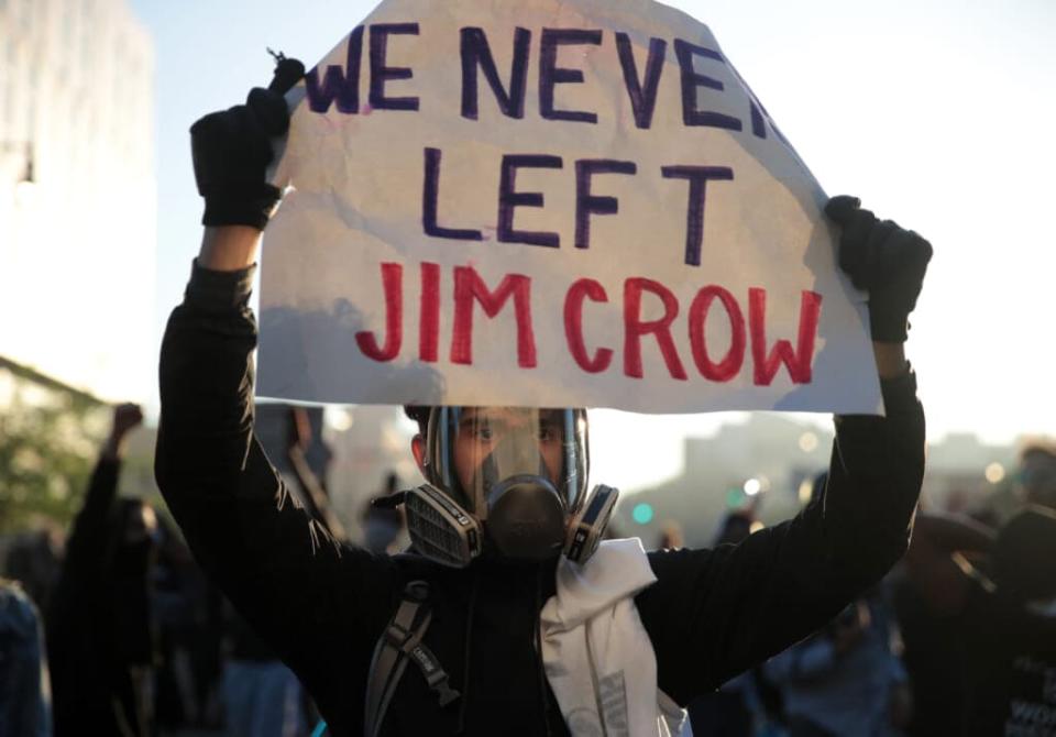 A protester holds up a sign that reads “We Never Left Jim Crow” during a protest sparked by the death of George Floyd while in police custody on May 29, 2020 in Minneapolis, Minnesota. (Photo by Scott Olson/Getty Images)