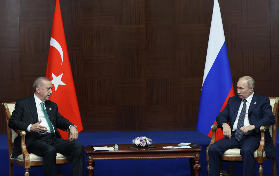 Turkish President Recep Tayyip Erdogan and Russian President Vladimir Putin sit with a small table between them at a meeting.