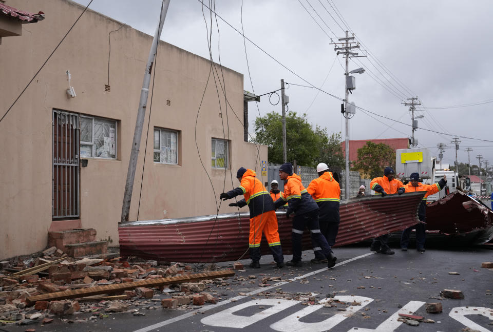 Rescue workers among damaged buildings in the Wynberg neighborhood of Cape Town, South Africa, Thursday, July 11, 2024. The area was hit overnight during strong winds that blew off roofs, destroyed parts of houses and other buildings, and brought down electricity poles. (AP Photo/Nardus Engelbrecht)