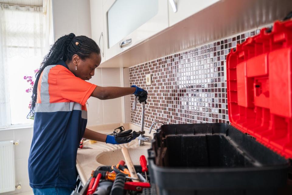 Female plumber with toolbox open troubleshooting water pressure at the kitchen sink